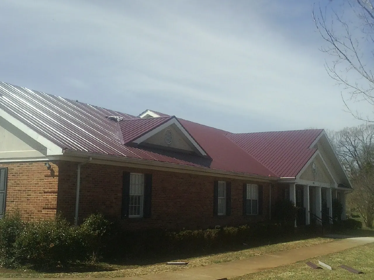 Red metal roof with gabled entries on a long brick building, from a Hail Damage Roof Repair job in Sandia Park