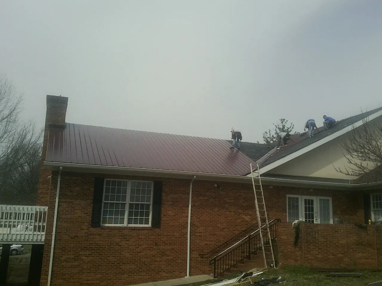 Crew setting red metal roofing panels on a brick home in Sandia Park