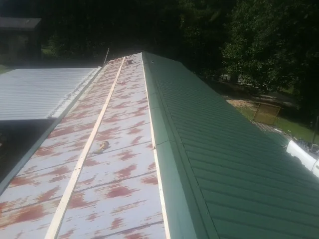 Old rusted panels beside newly installed green metal roofing — Wind Damage Roof Repair by Roofing Brothers in Sandia Park