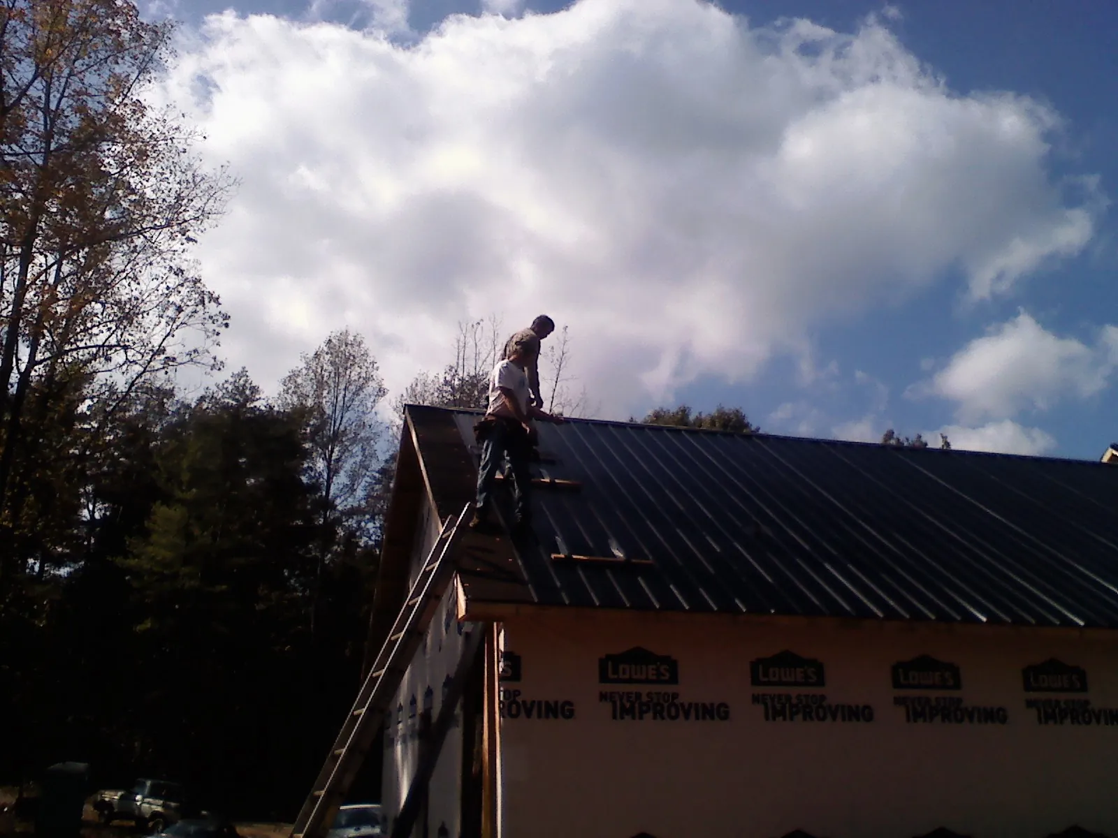 Roofer fastening dark metal panels high against a cloudy sky, from a Roof Inspection job in Sandia Park
