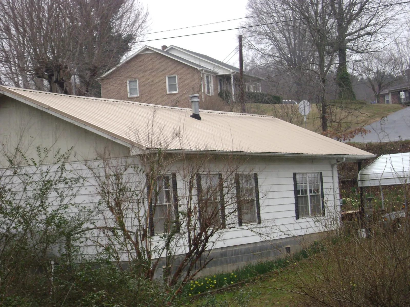 Tan metal roof on a white sided house set into a hillside — Commercial Roofing by Roofing Brothers in Sandia Park